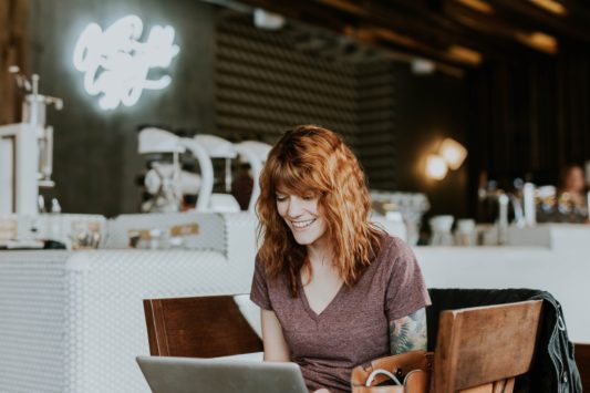 Woman in coffee shop on laptop building her side hustle.