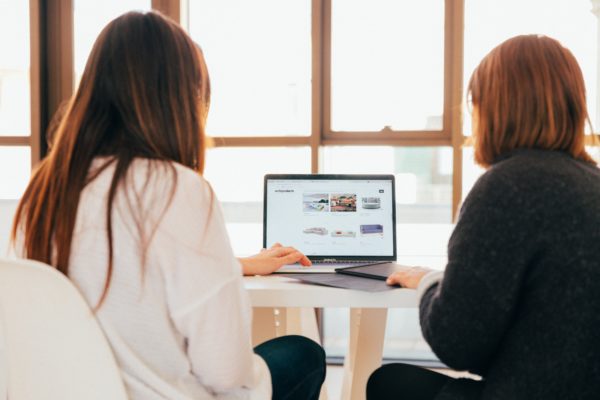 Two women looking at a laptop while starting a side hustle.