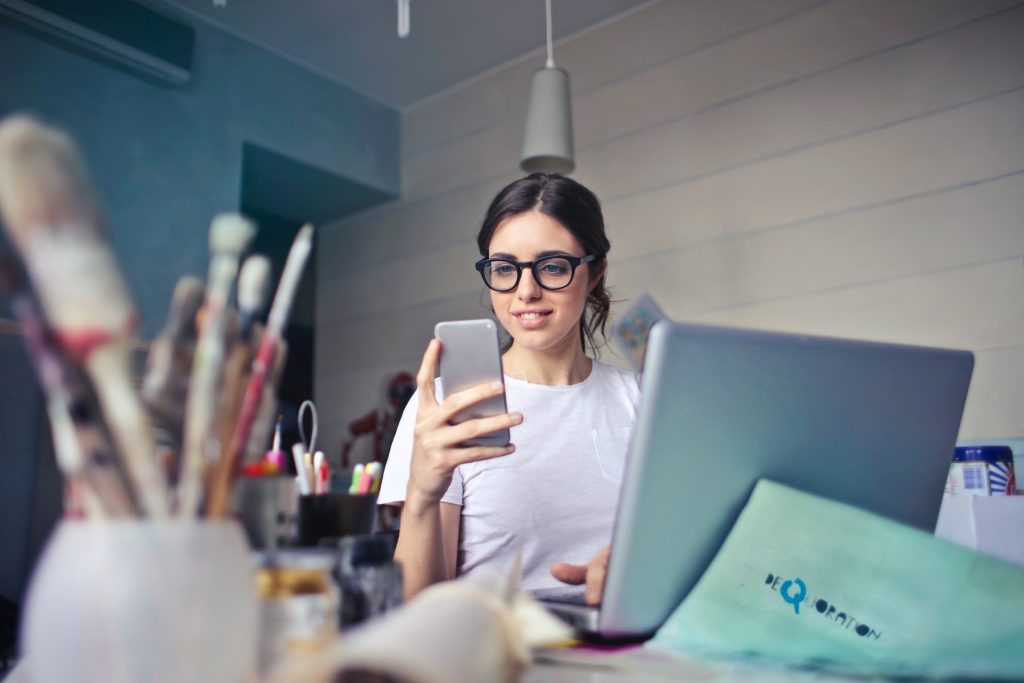 A woman checking her phone while working on her laptop