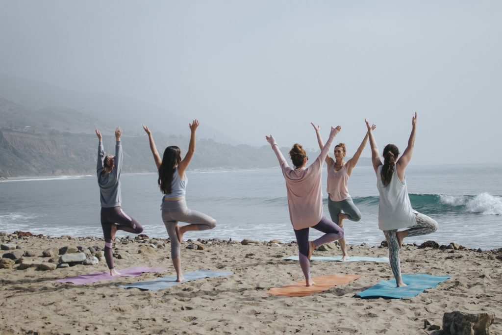 5 woman having a yoga session on the beach
