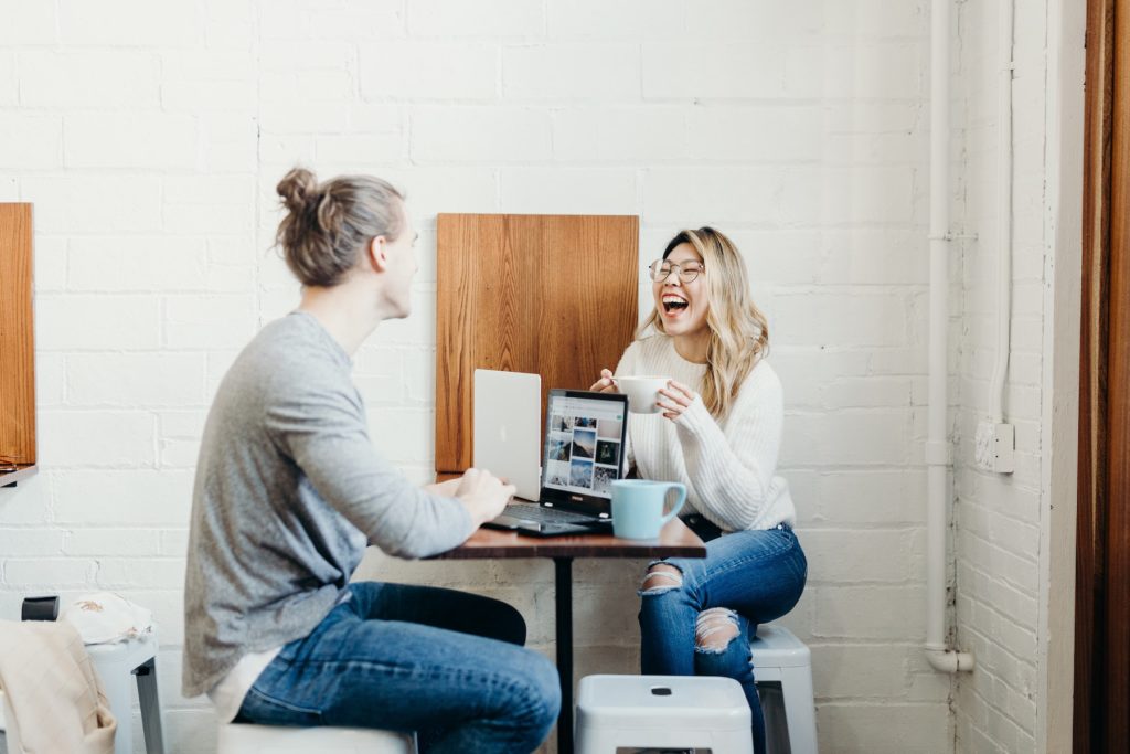 A woman and a man working and laughing over a cup of coffee 