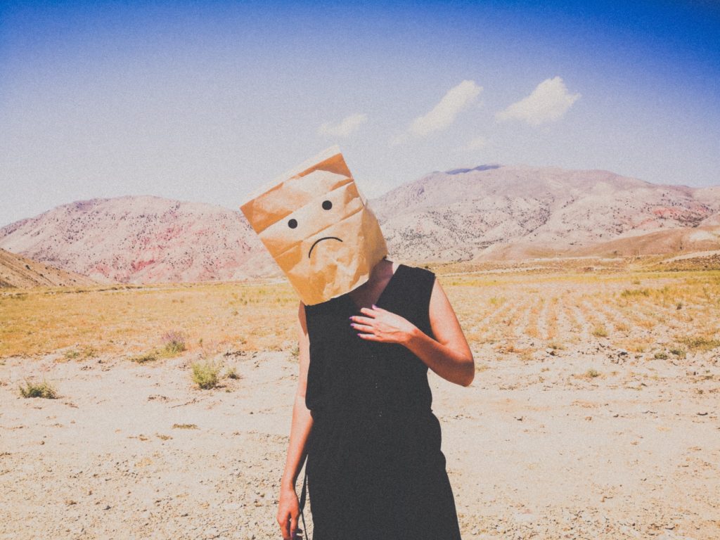 A person with a sad paper bag as a mask
