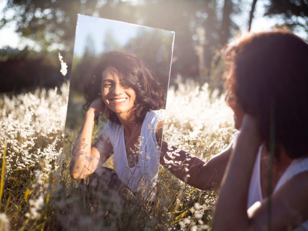 A woman smiling in a mirror in a field
