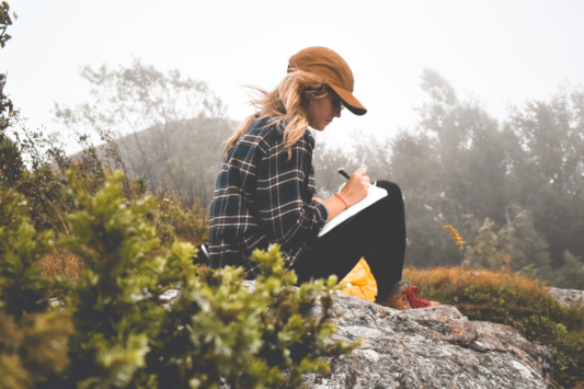 woman outside sitting on a rock journaling