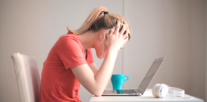 woman upset looking down at computer holding her head