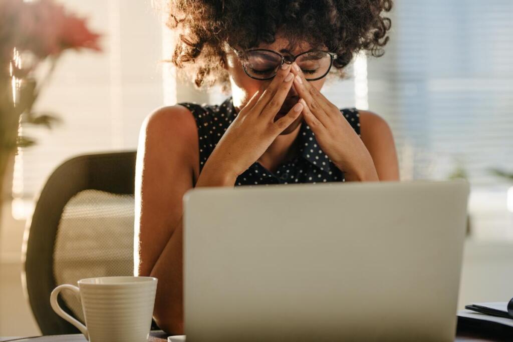 frustrated woman looking down at computer with her head in her hands