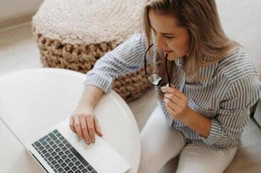 Woman on laptop holding reading glasses to her mouth