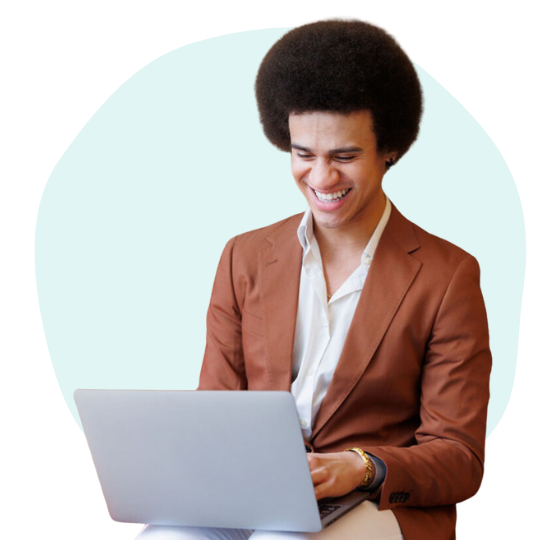 a young man in a blazer smiling while working on his laptop