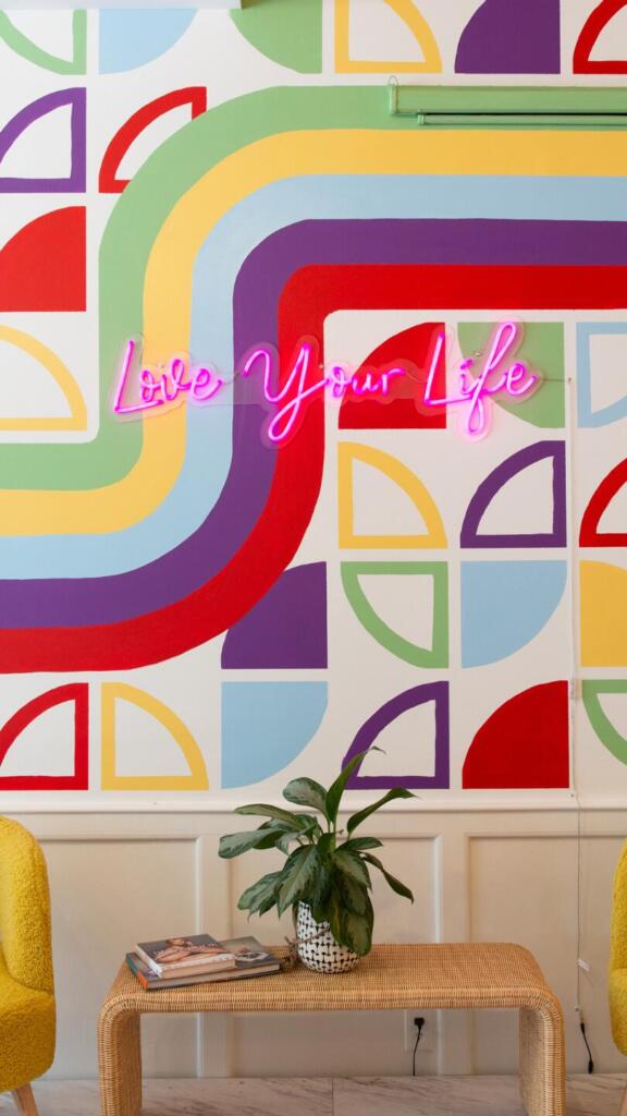 "Love your life" neon sign on graphic wall of Ama La Vida's Chicago office