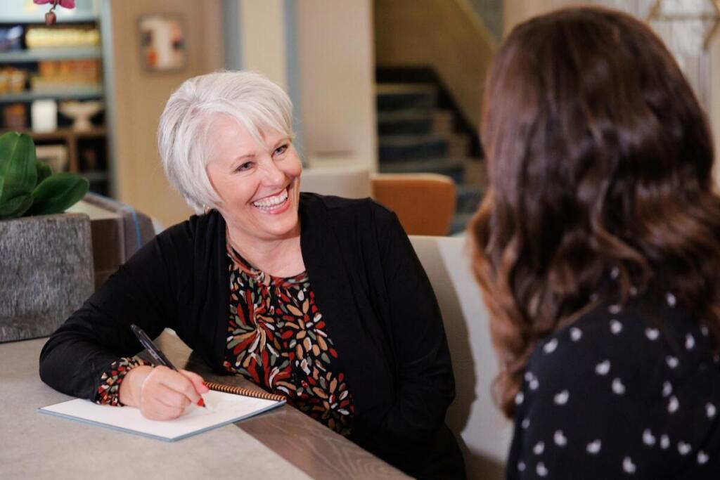 Woman smiling while talking to another woman, taking notes