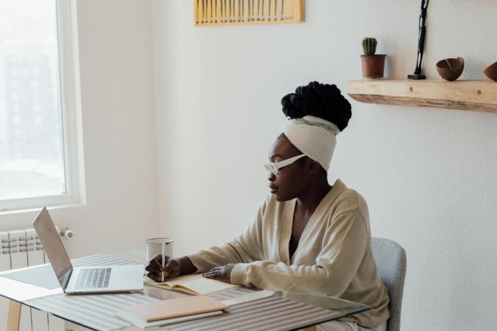 Woman writing in journal and looking at laptop