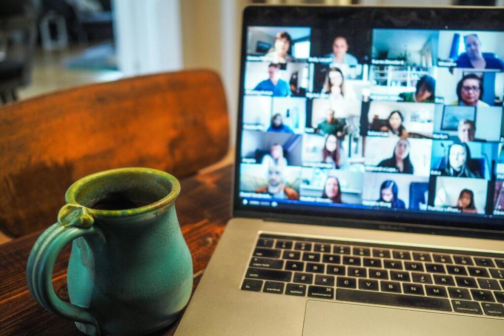 Coffee mug and laptop with virtual meeting with many people's faces on the screen