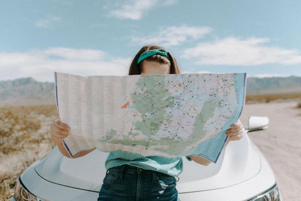 woman looking at a map while leaning on her car pulled over on the side of the road