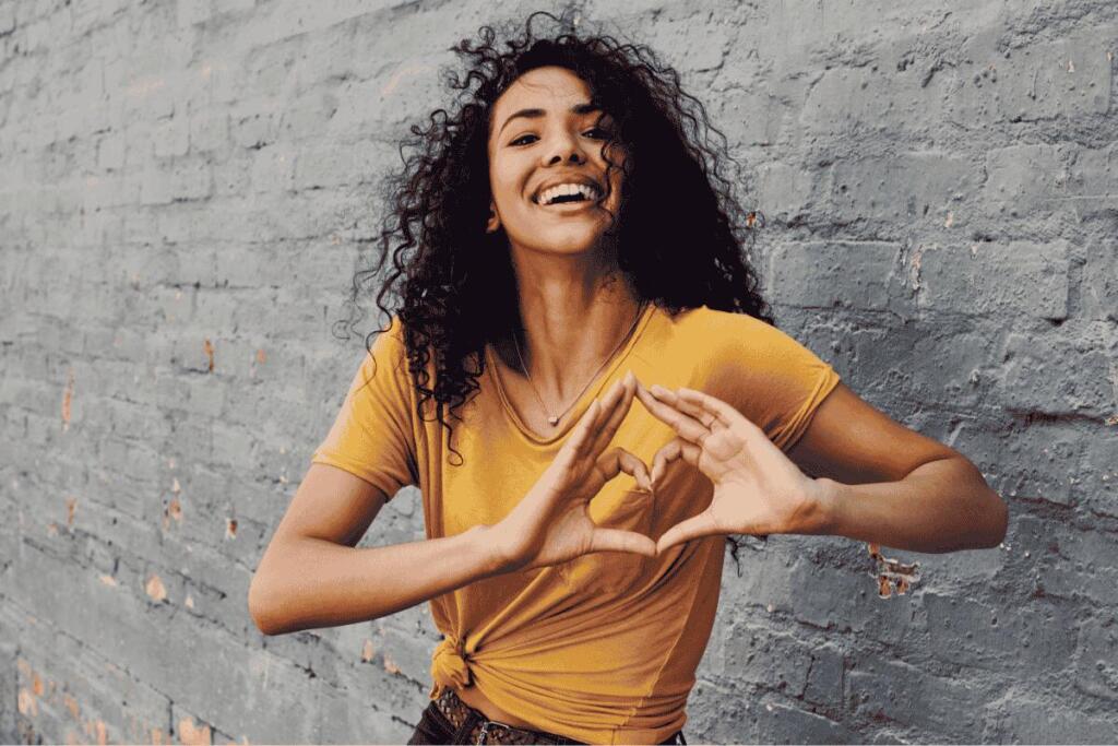 Woman with curly hair making a heart with her hands.
